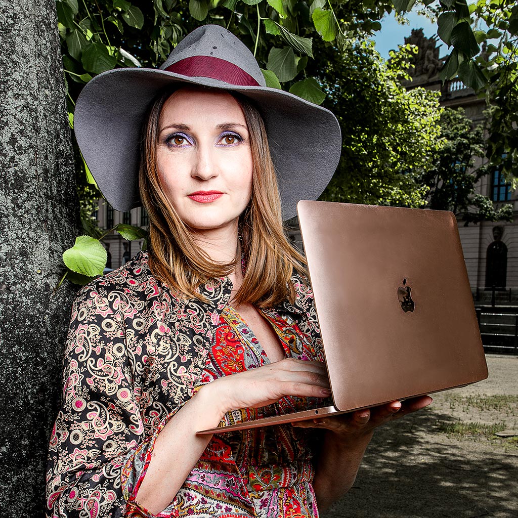 Frau steht und hält einen Macbook in der Hand