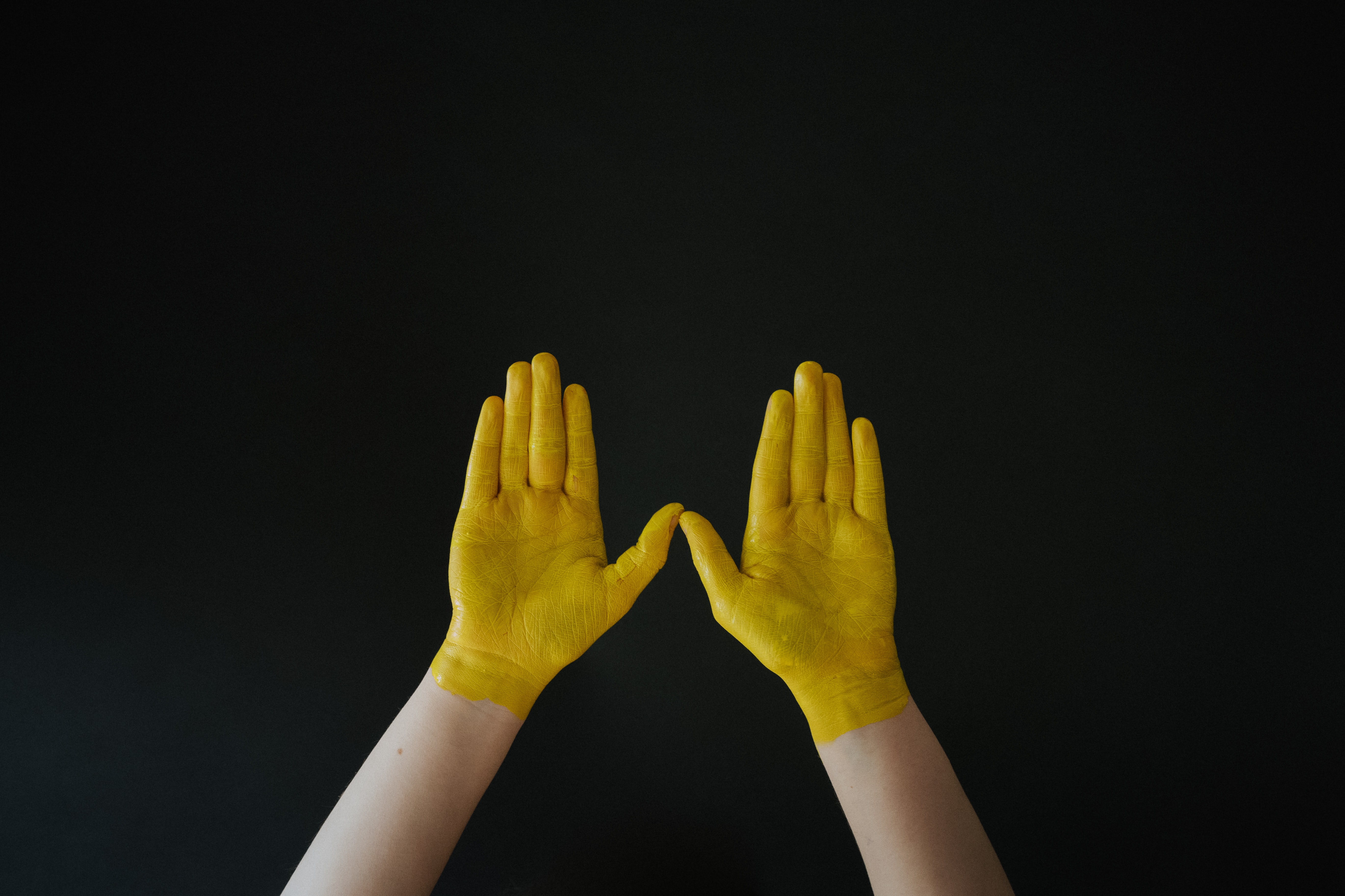 Zwei gelb angemalte Hände vor schwarzem Hintergrund